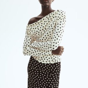 Un haut à manches longues épaules dénudées en crème avec des pois noirs, doté d'un col drapé, est associé à une jupe midi noire ajustée ornée de pois crème et d'un léger froncement latéral.